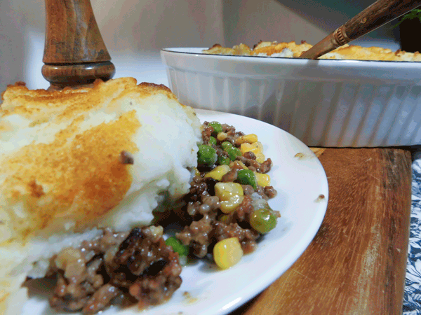 Cut away view of cottage pie on a white plate mounded with mashed potatoes