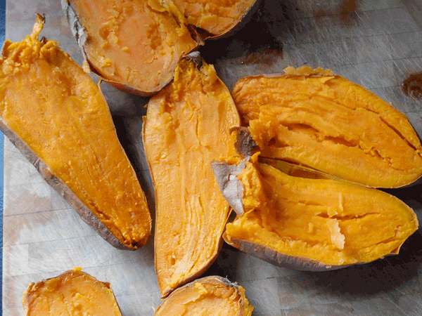 Baked sweet potatoes split in half on a chopping block