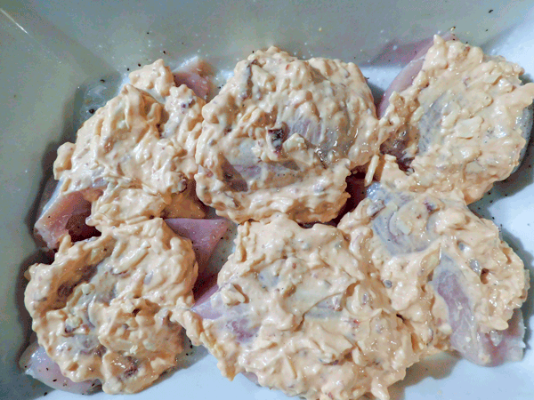 Raw chicken in a white casserole dish with cheese mixture spread on top