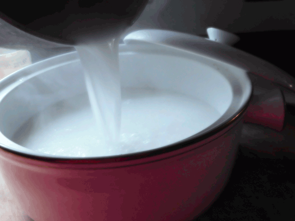 Rice in casserole with coconut milk pouring in 