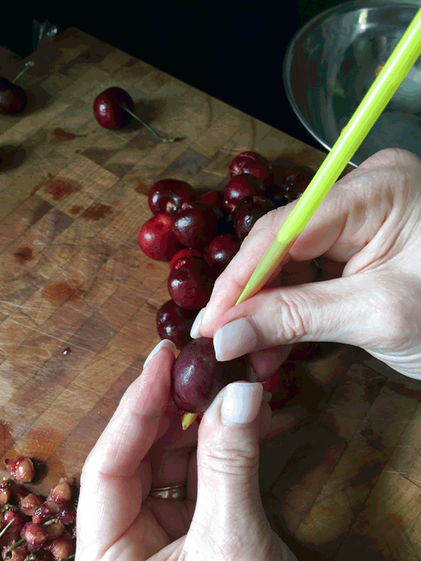 Pitting cherries with a straw over a chopping board