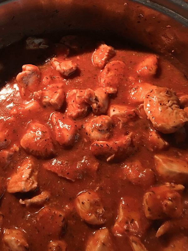 Chicken in a red sauce cooking on the stove