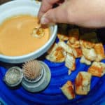 Firecracker Chicken Bites on blue plate with white bowl of dip with a hand getting a piece.