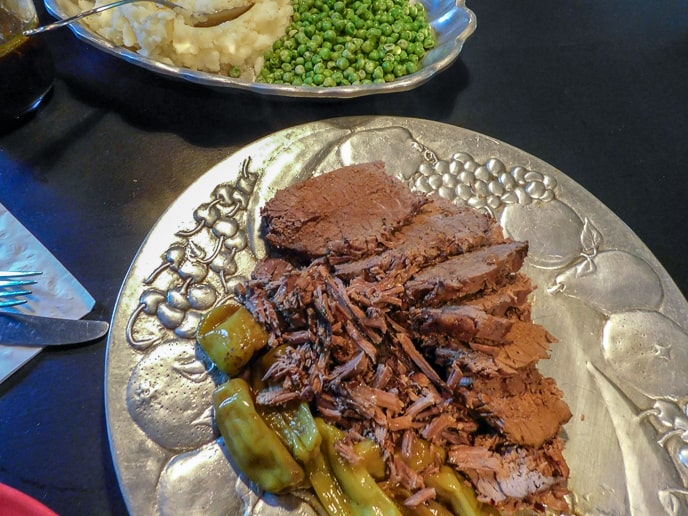 Pot Roast on a silver platter with a bowl of peas and mashed potatoes