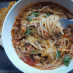 White bowl with sausage and noodles in broth on a chopping block with toasted bread