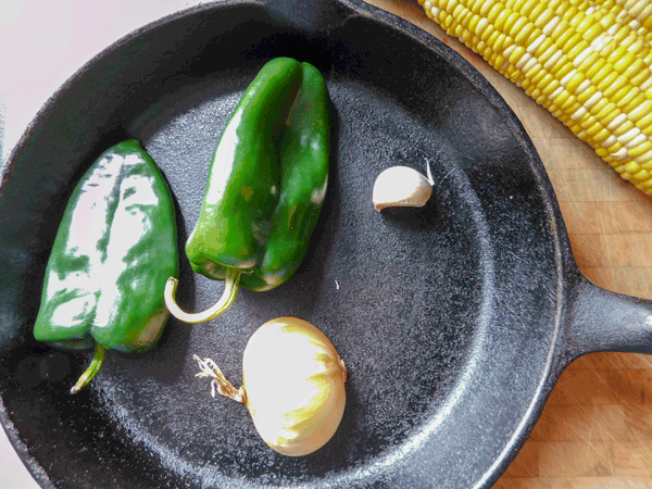Green Peppers onion and garlic in a skillet next to corn on cob