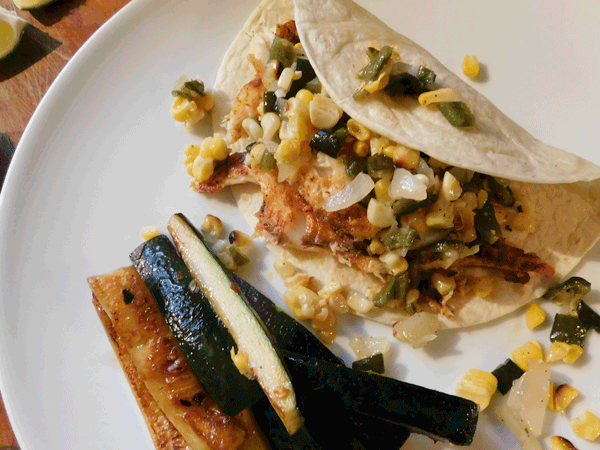 Cooked Fish filet in a flour tortilla with corn and green pepper salsa on a white plate with sauteed zuchini