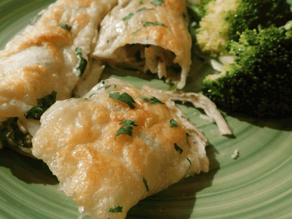 Crispy chicken enchiladas suizas on a green plate with broccoli