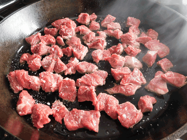 Cubes of beef searing in cast iron skillet