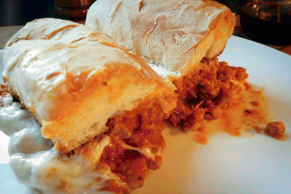 Sausage in tomato sauce on a hoagie bun with cheese on a white plate