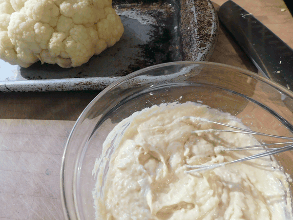 head of cauliflower on baking dish with white mixture next to it on chopping block