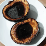 Two sides of roasted acorn squash with dark syrup in cavity on white plate