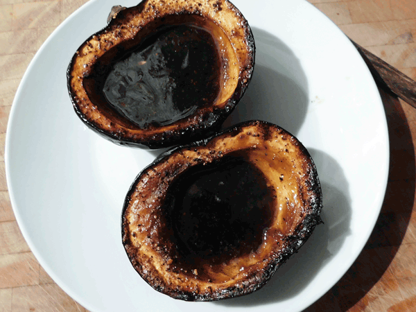 Two sides of roasted acorn squash with dark syrup in cavity on white plate