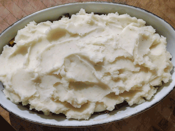 Top view of mashed potatoes on top of ground beef in a caserole dish