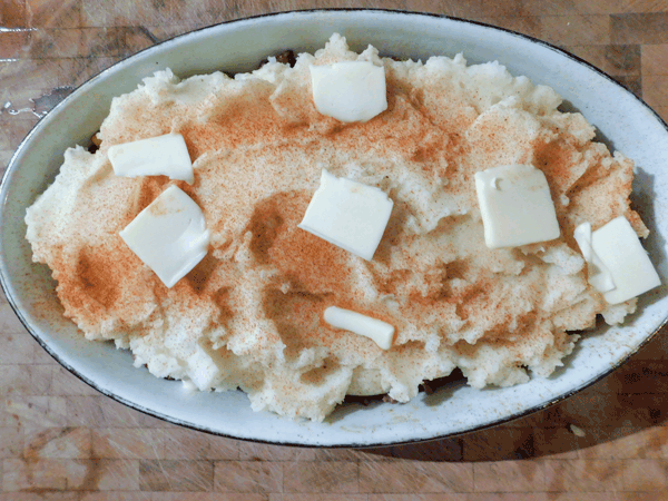 Mashed potatoes in white oval casserole dish dotted with butter and sprinkled with paprika
