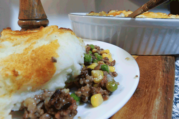 Cut away view of cottage pie on a white plate mounded with mashed potatoes