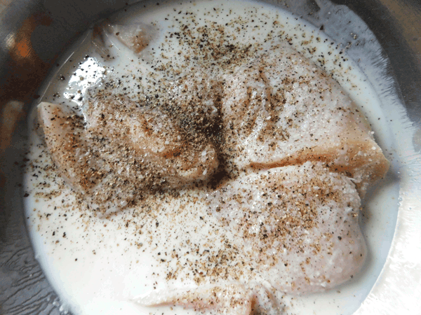 Raw Chicken Breasts in buttermilk in a mixing bowl