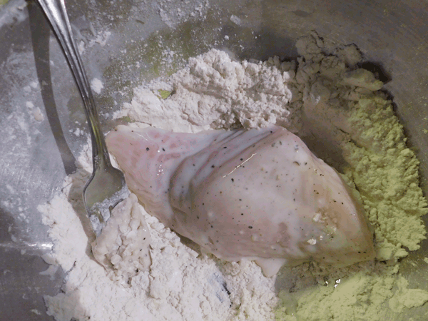 Marinated chicken getting dredged in flour in mixing bowl