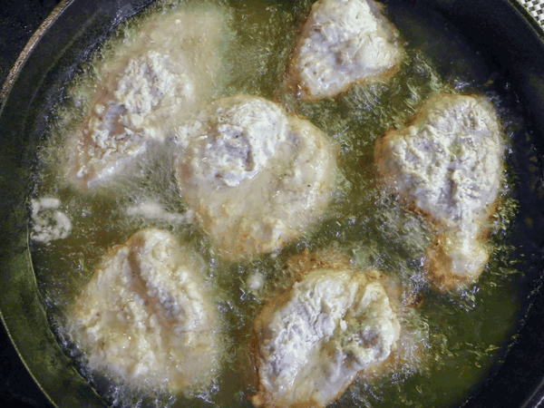 Breaded chicken cooking in oil in cast iron pan
