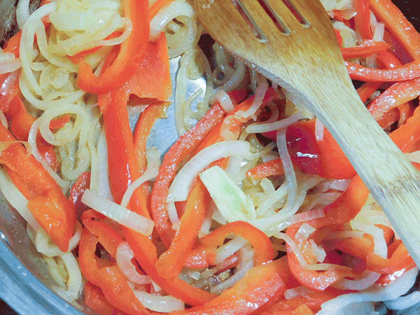 Sliced red peppers and onions sauteing in a pan