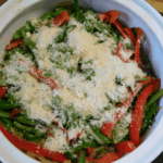 green beans, red peppers and onions in a casserole covered in parmesan cheese