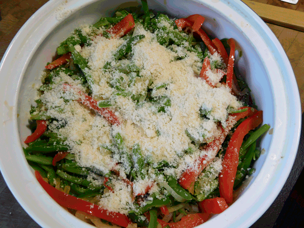 green beans, red peppers and onions in a casserole covered in parmesan cheese