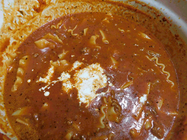 Red soup base with lasagna noodles in a white dutch oven