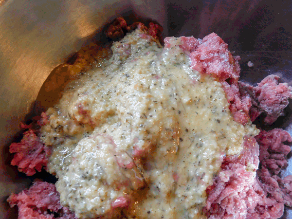 Ground meat with meatball ingredients poured over top in a metal bowl
