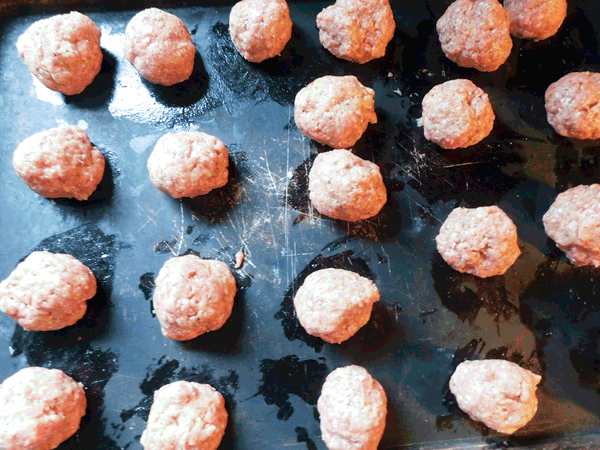 Small uncooked meatballs on a black baking sheet