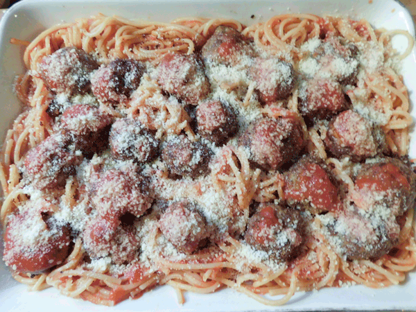 Spaghetti with meatballs on top in a casserole dish covered with parmesan cheese