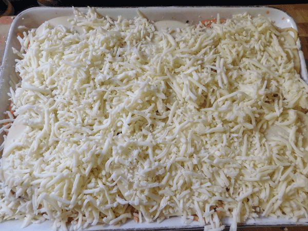 White casserole dish with uncooked cheese over spaghetti