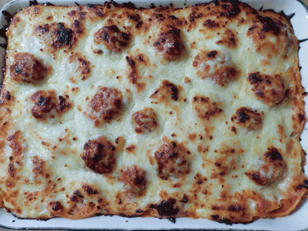 White casserole dish with cooked cheese over meatballs