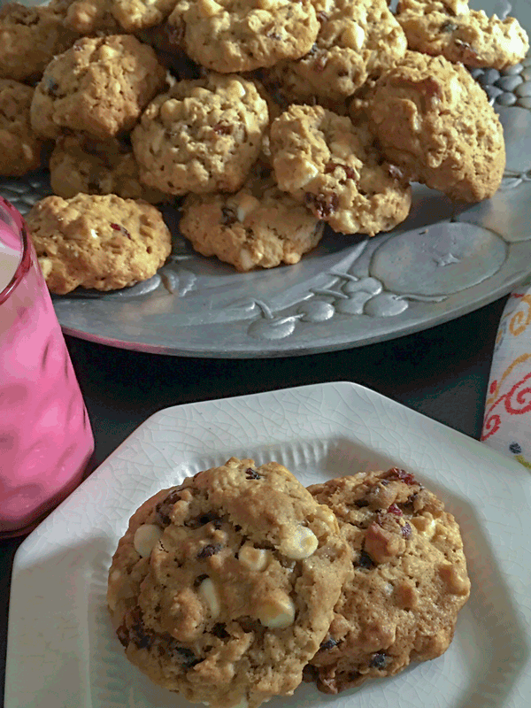 Platter of fully loaded cookies next to a white plate of cookies and a pink glass of milk