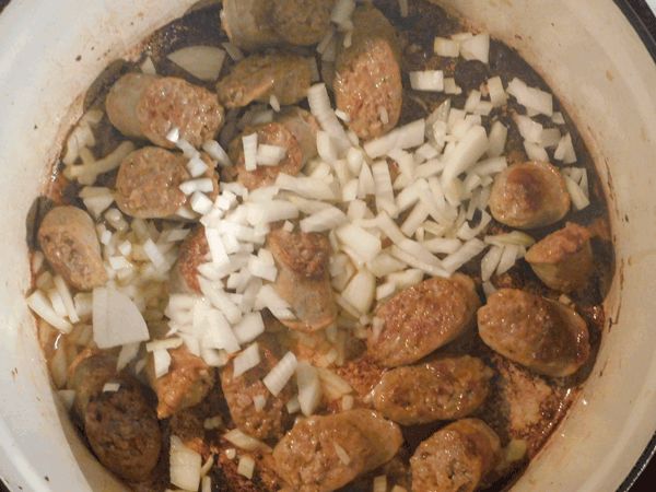 Cooked diagonally sliced sausage in a soup pot with chopped onions