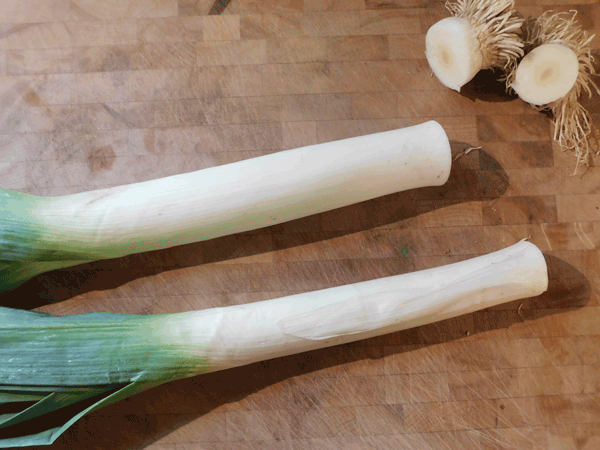Two leeks on a chopping board with the tops cut off