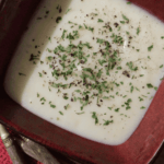 Creamy Potato Leek Soup in a red bowl with pepper and parsley sprinkled on top