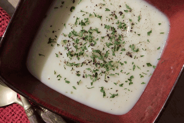 Creamy Potato Leek Soup in a red bowl with pepper and parsley sprinkled on top