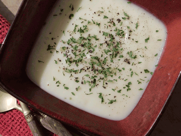 Creamy Potato Leek Soup in a red bowl with pepper and parsley sprinkled on top