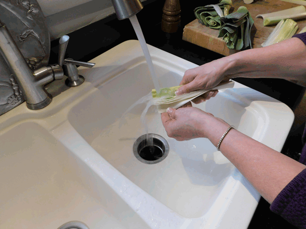 Hands cleaning a piece of leek over white sink with water running over