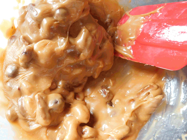 Melted caramel and nuts in a glass bowl with a red spatula