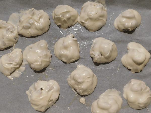 Caramel nut clusters coated with white chocolate on parchment lined cookie sheet