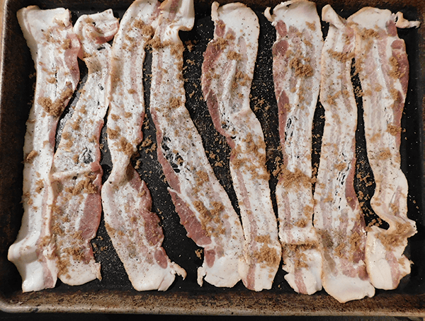 Raw bacon on a baking sheet with brown sugar sprinkled on top