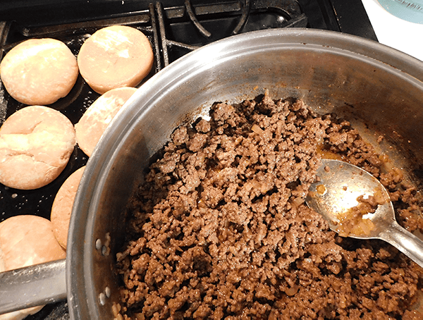 cooked ground beef in a skillet next to buns grilling on a griddle