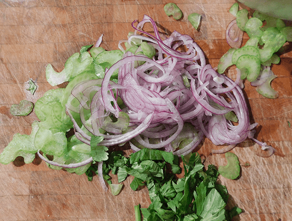 thin slices of red onions and celery on a chopping block