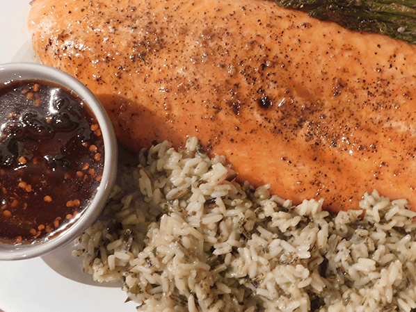 large salmon filet cooked with maple glaze and a side of rice and glaze in a cup