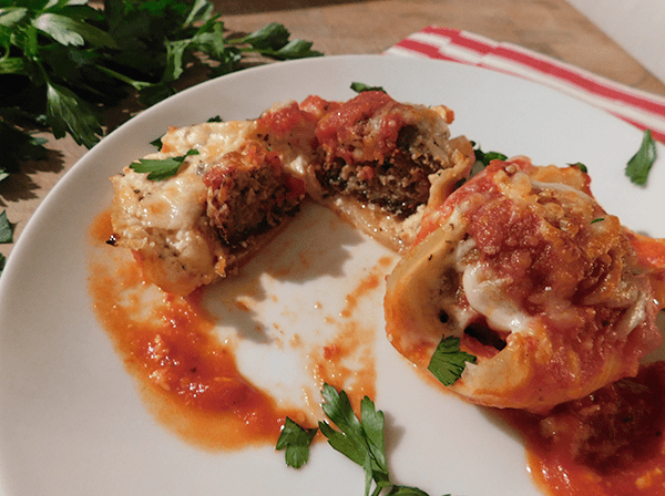 Two double stuffed shells on a plate with one cut open