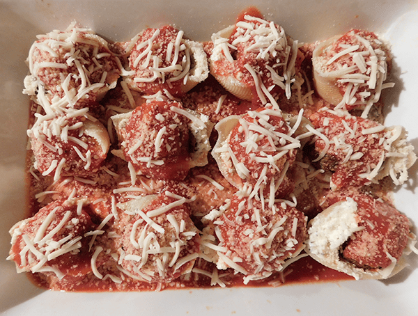 Meatball stuffed shells in casserole on top of tomato sauce, covered with shredded cheese