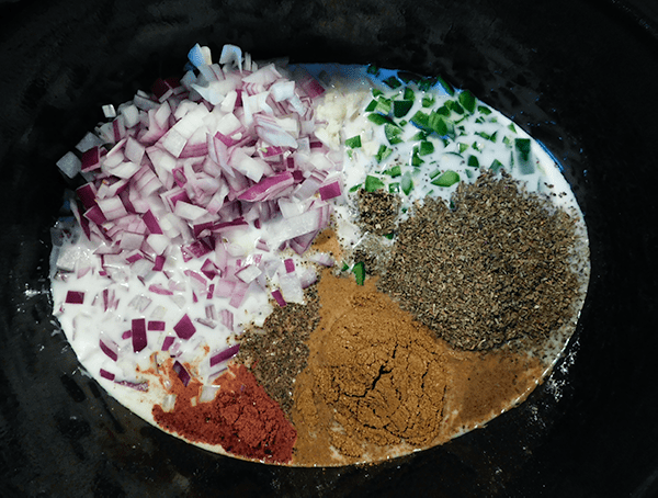 Red onions, jalapenos and spices in slow cooker in a pool of coconut milk
