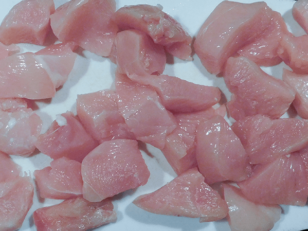 Raw boneless chicken breast cut into pieces on a white board