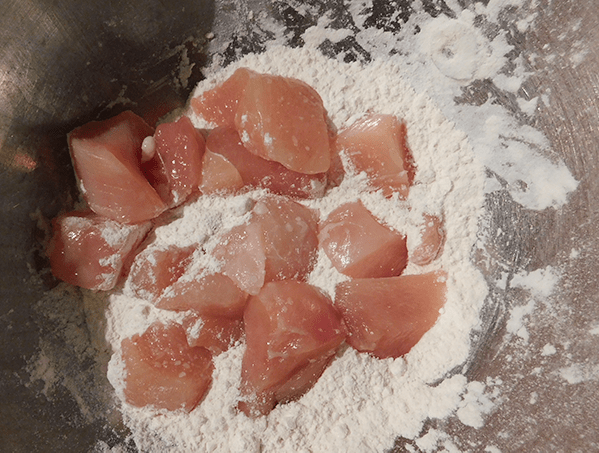 Raw chunks of chicken breast in flour in a metal bowl